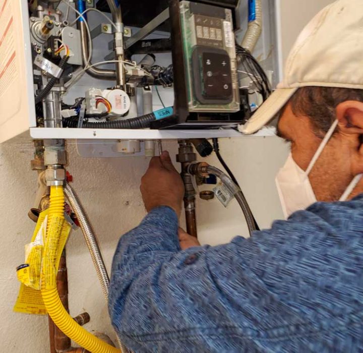 Technician adjusting valves on a modern water heater, showing intricate pipework and digital control units.