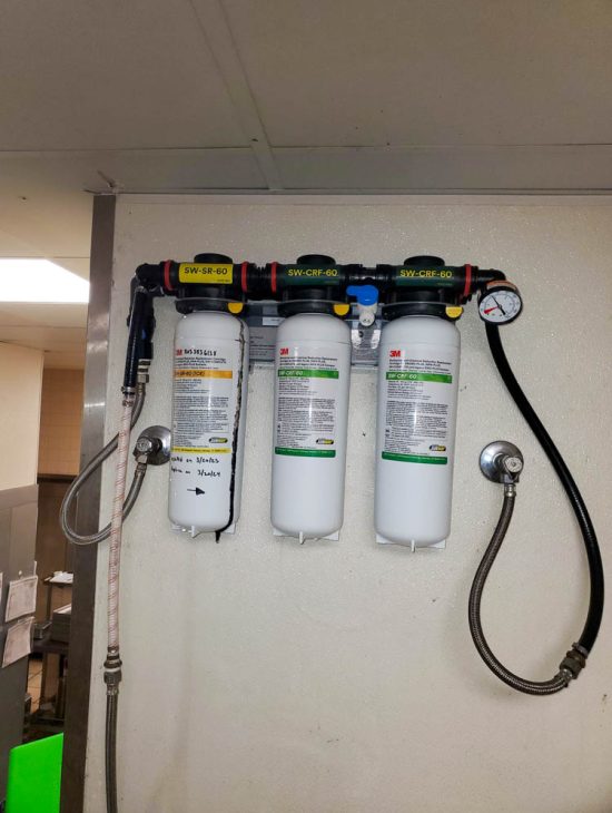 Advanced Water Filtration System Installation Industrial water filtration system mounted on a wall with three large white canisters, equipped with pressure gauges and metal piping.