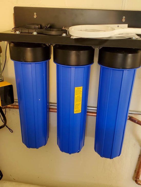 Large Scale Water Purification Installation Three large blue water purification tanks installed in a utility room, connected to a complex array of pipes and gauges.
