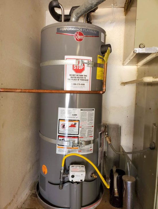 Residential High-Capacity Water Heater Rheem Performance Platinum water heater installed in a utility area, complete with safety stickers and gas connection.