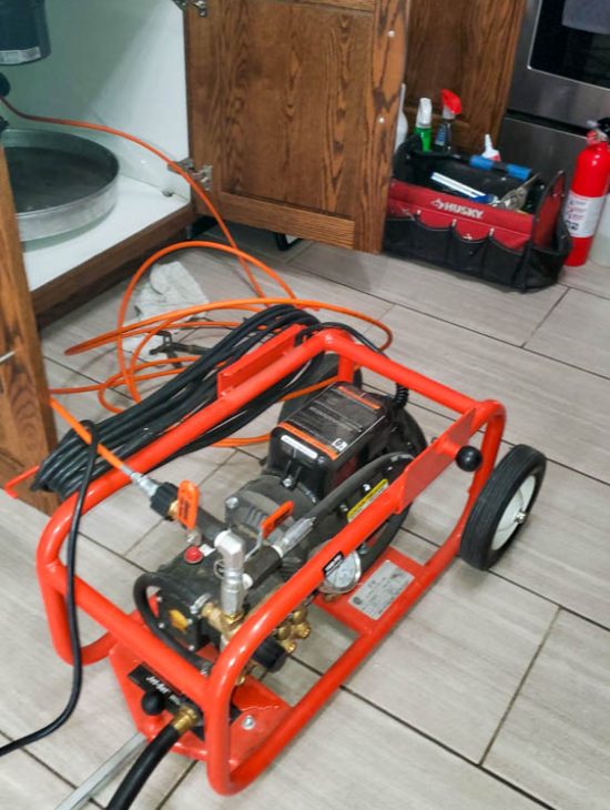 Compact Hydro-Jetting Machine Compact hydro-jetting machine placed on a bathroom floor, equipped with hoses and fittings, illustrating modern plumbing tools in use.