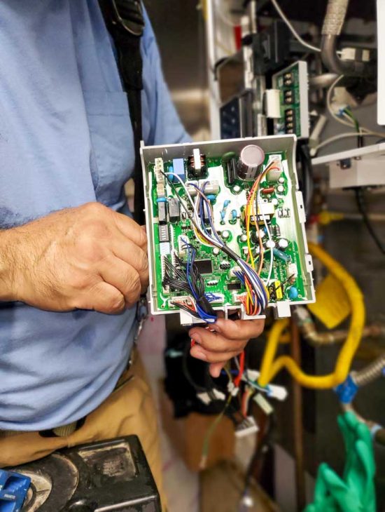 Technician Examining Boiler Circuitry Close-up of a technician's hands working on the electronic circuit board of a boiler, highlighting complex wiring.