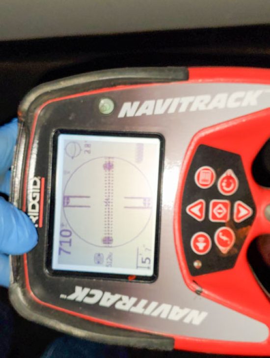 Precision Pipe Locator Tool Hand holding a RIDGID Navitrack precision pipe locator, demonstrating technology used for detecting underground pipes.