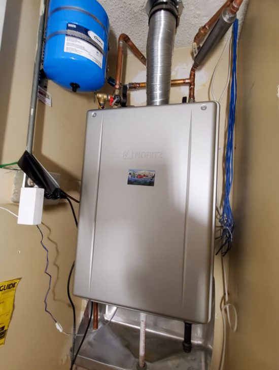 Compact Tankless Water Heater Installation Noritz tankless water heater setup with expansion tank and ventilation in a small utility closet, enhancing space efficiency.