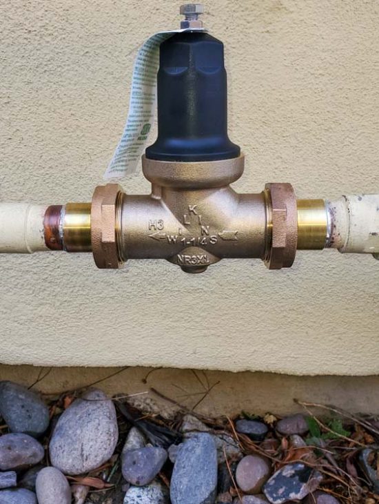 Water Pressure Regulator on Exterior Pipeline Close-up of a water pressure regulator with a gauge installed on an outdoor water pipeline.
