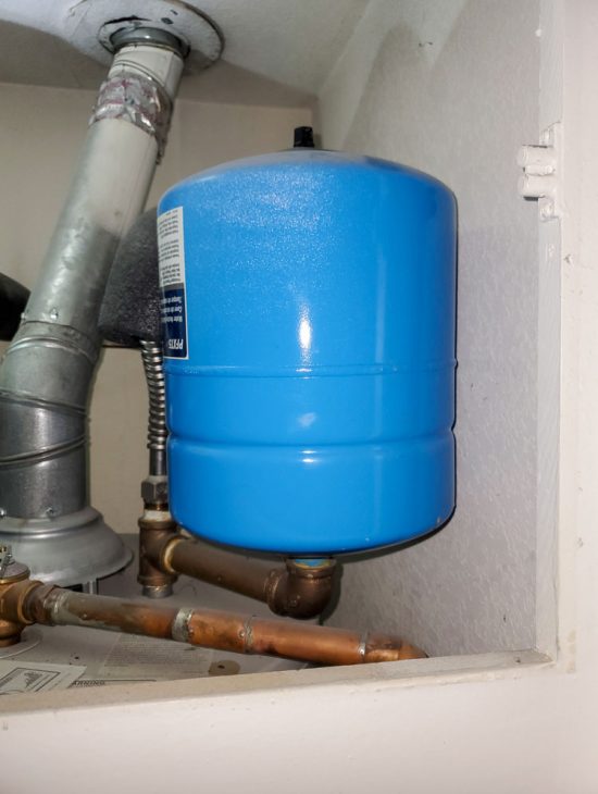 Pressure Tank Installation for Water System Blue pressure tank installed under a utility sink, connected to a water filtration system.