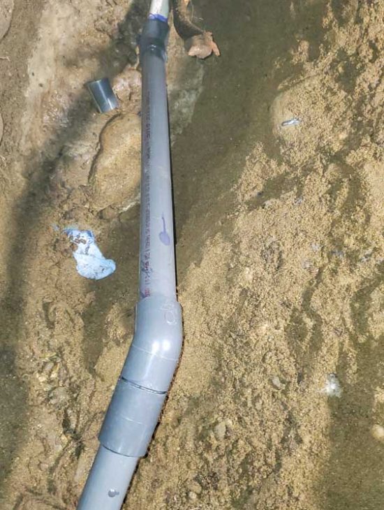 Exposed Water Pipe Repair A damaged water pipe partially buried in sandy soil, with repair sections visible.