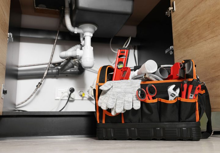 A well-equipped plumbing toolbox with various tools displayed under a kitchen sink, ready for maintenance work.